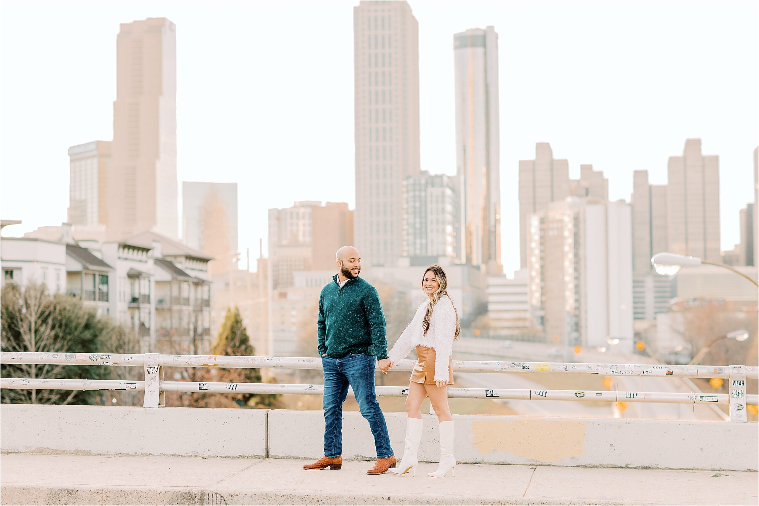 couple walking across bridge with Atlanta skyline in background  