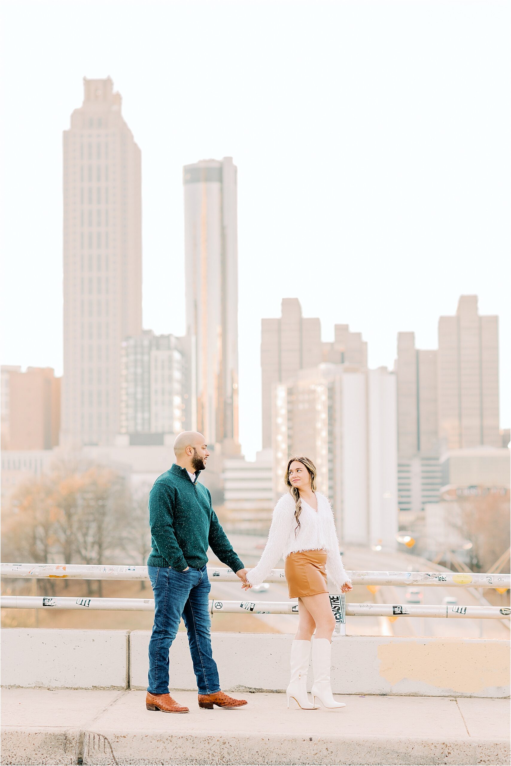 couple walking across bridge with Atlanta skyline in the background  