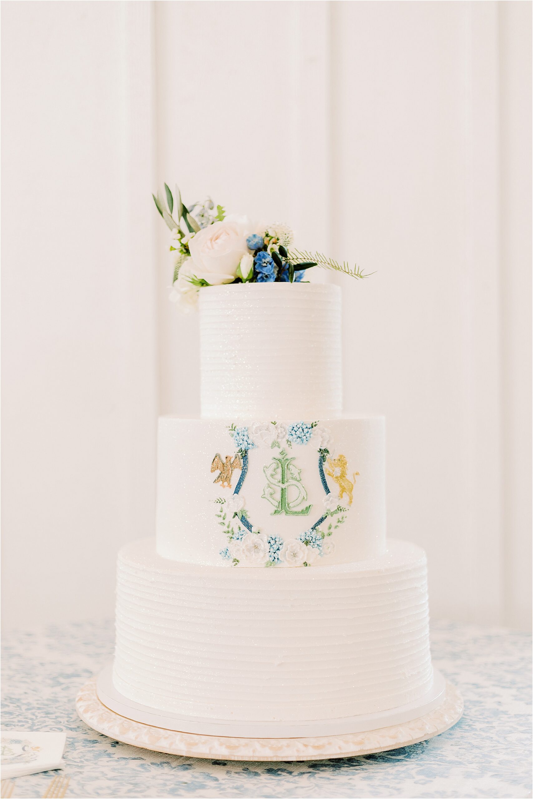 White cake with flower on top and crest on middle tear. 