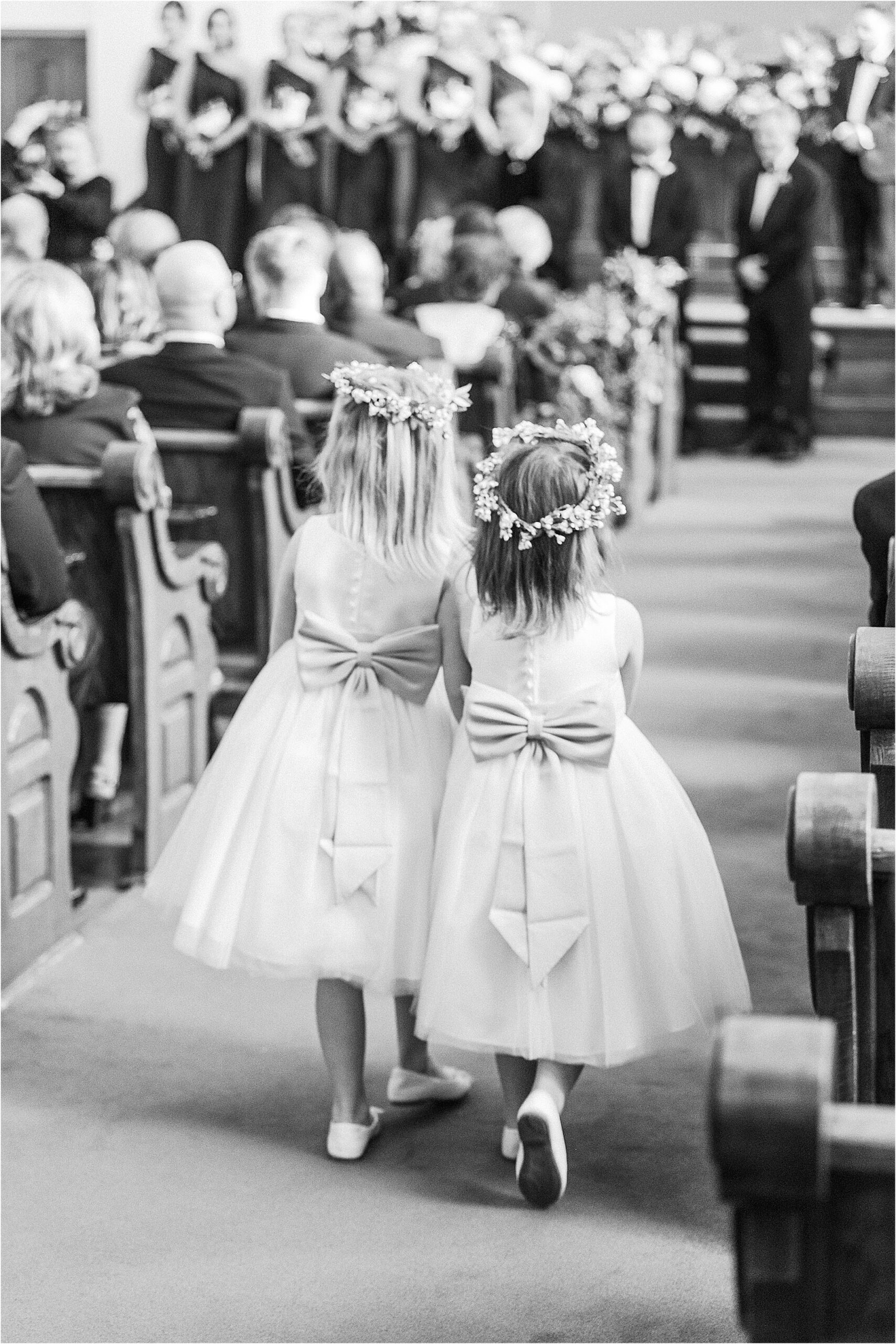 Black and white image of flower girls walking down the aisle of church. 