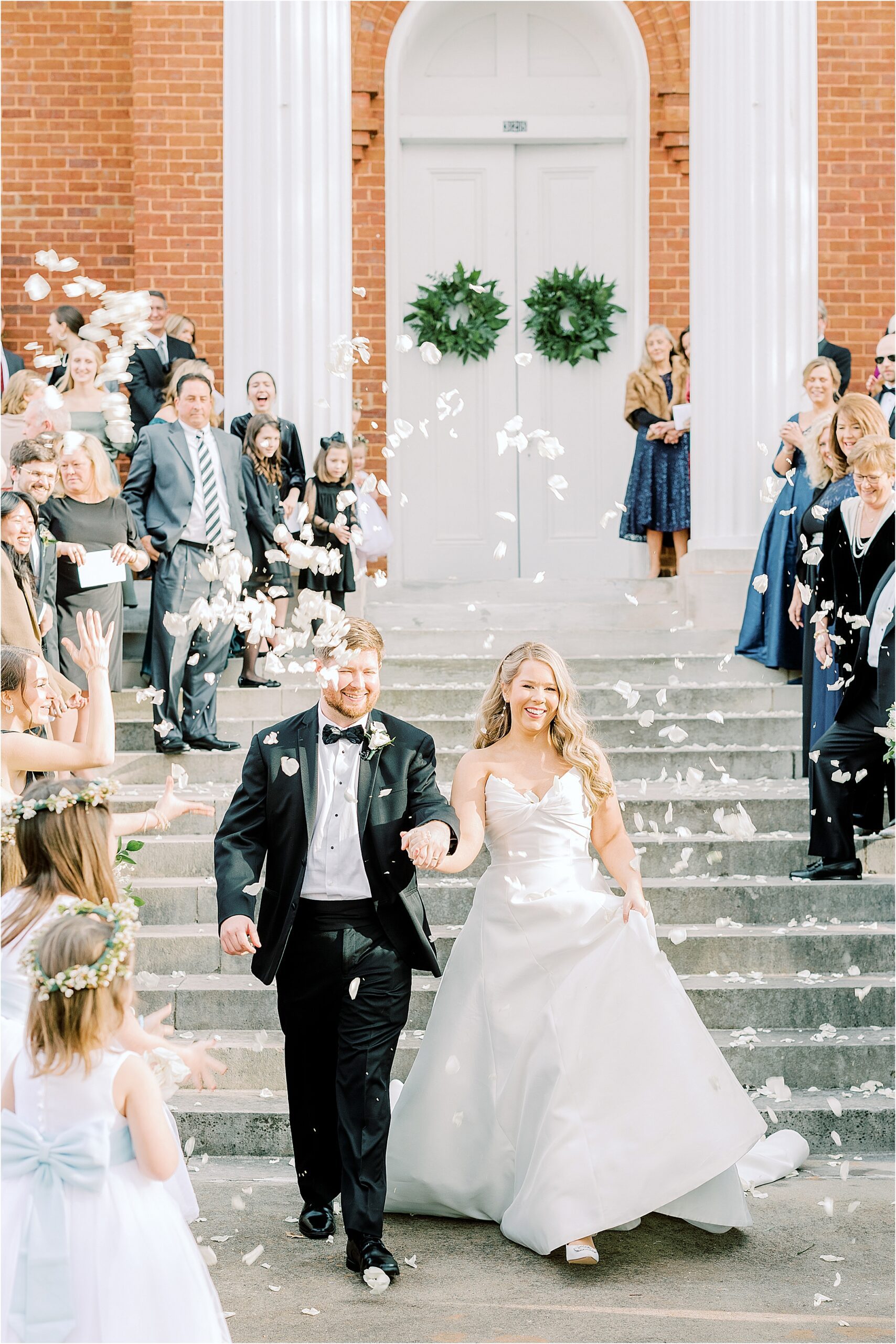 Bride and groom leaving brick church, guest throwing flower petals. 