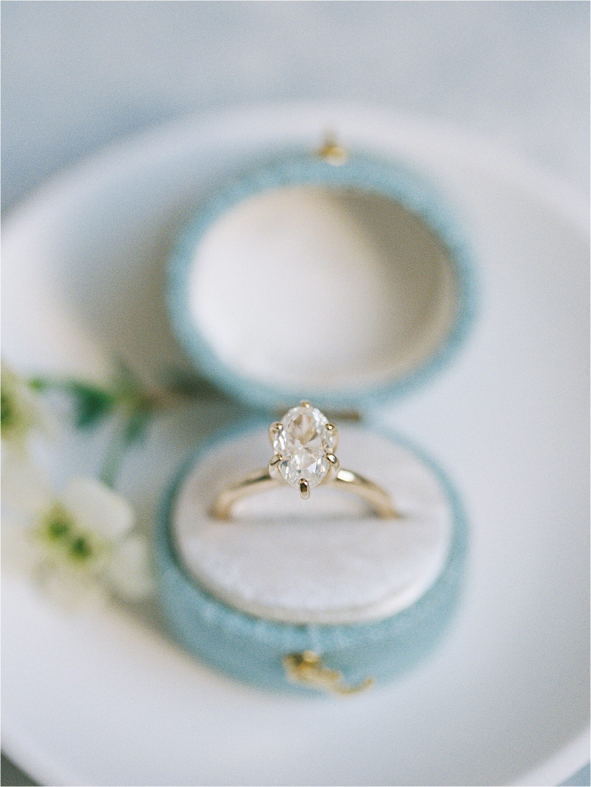A diamond ring in a blue ring box sitting on a white plate.