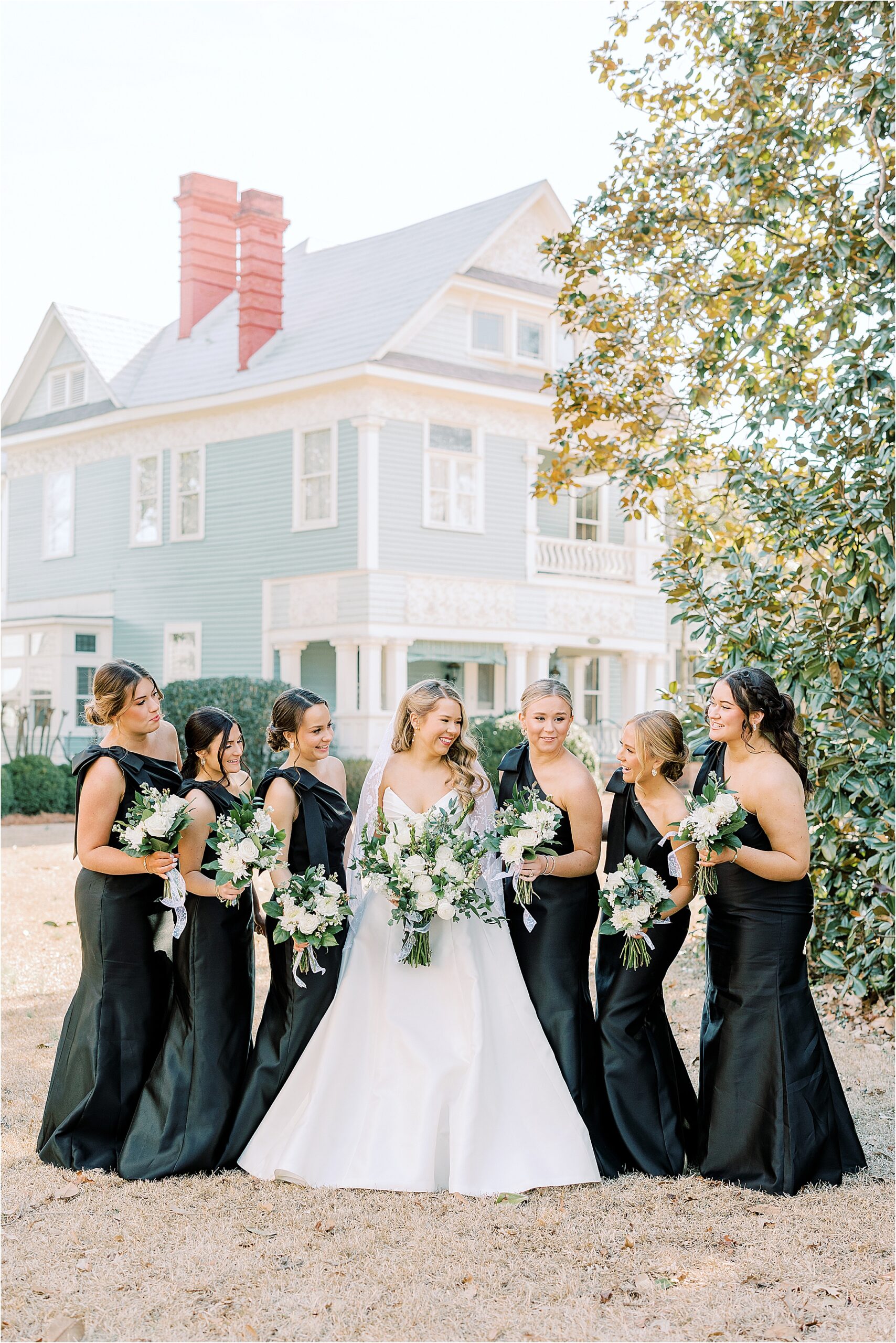 Bride in a white dress, bridesmaids in black dresses holding flowers and looking at one another